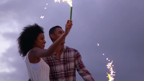Couple jouant avec des cierges magiques sur la plage au crépuscule 4k