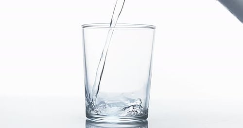 900033 Se vierte agua en un vaso sobre un fondo blanco, Cámara lenta 4K