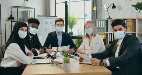 Multiracial Businesspeople in Protective Masks Looking Into Camera in Office Room