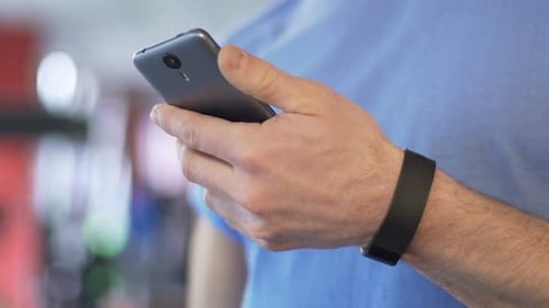 Male Scrolling Down Screen of Mobile Phone in Gym Before Start of Workout