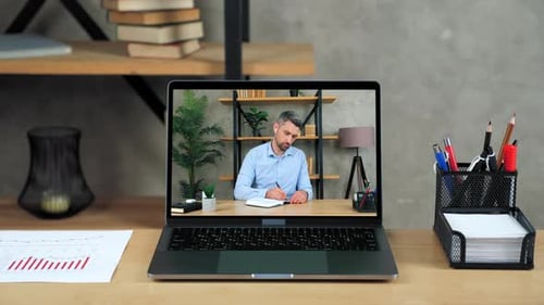 Laptop Standing on Table Display with Businessman in Office Writes in Notebook