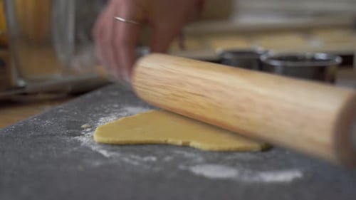 Woman using wooden rolling pin to flatten dough and using cookie cutters to make simple, homemade co