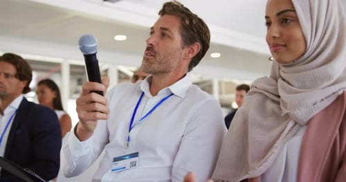 Man Speaking Into Microphone at Conference With Audience