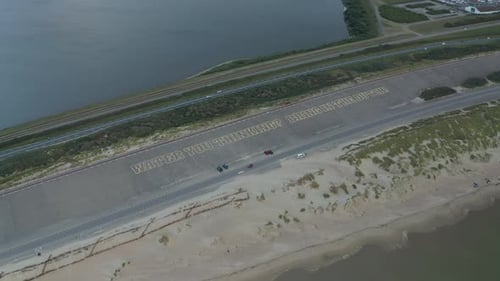Großes Schild auf dem Parkplatz mit der Aufschrift „Wasser denkst du? Bring die Holländer rein! „In Strandnähe, Luftaufnahme