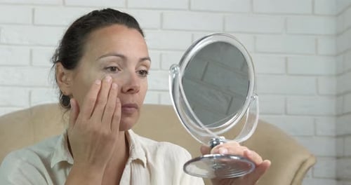 Woman Massaging Face While Looking in Mirror