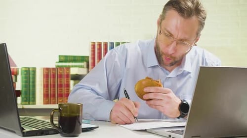 40 Years Old Man is Hardworking in the Office Eats Unhealthy Food Deadline Concept