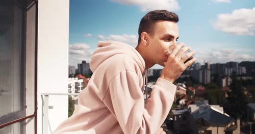 Young Adult Drinking on Balcony Overlooking City