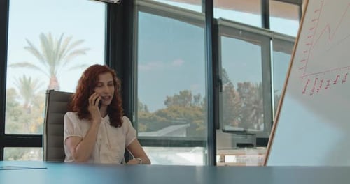 A business woman with ginger hair talking on the phone while sitting in her office. Slow motion.