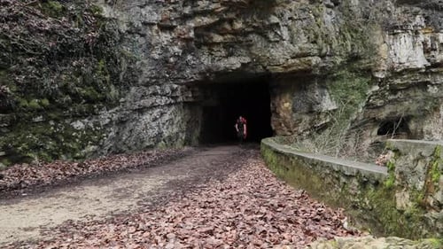 Single male backpacker walking out of a mountain tunnel on hiking path outdoors