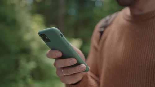 Nahaufnahme eines Mobiltelefons in den Händen eines männlichen Reisenden, der durch den Wald geht