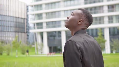 Un jeune homme noir regarde autour de lui - Des immeubles de bureaux dans un arrière-plan flou