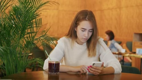 Joyful Girl Drinking Tea in a Cafe and Talking on the Phone or Video Call