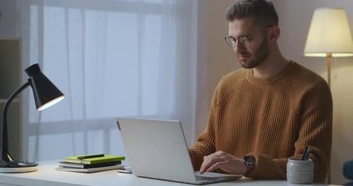 Erwachsener Mann tippt und sendet Nachrichten über das Internet über den Laptop, der im Wohnzimmer sitzt und soziale Netzwerke nutzt