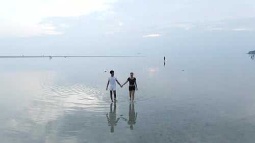 Romantic Happy Interracial Couple Walking on a Beach in Shallow Sea Water at Sunset Holding Hands