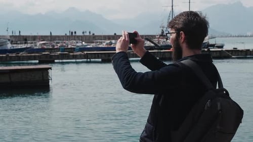 Man Taking Photo by Waterfront in Harbor on Sunny Day