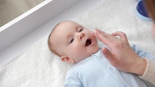 Infant Receiving Lotion on Face Lying on Blanket