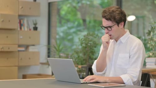 Young Man Coughing While Using Laptop in Modern Office