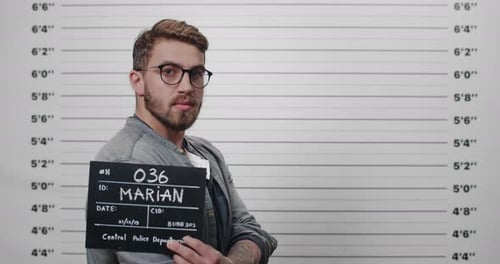 Mugshot de profil latéral d'un homme à la barbe et à la moustache tenant une pancarte