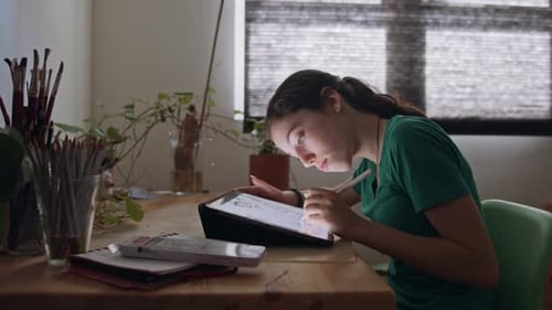 Young Woman Drawing on Tablet at Wooden Table