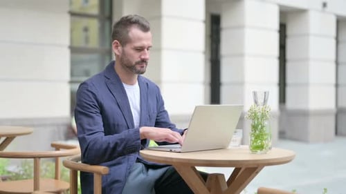 Man Working on Laptop While Sitting in Outdoor Cafe