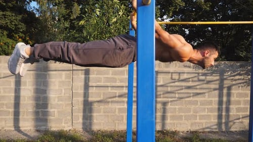 Strong Sporty Man Showing Some Gymnastics Stunts on Horizontal Bar Outdoor
