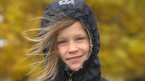 Blond Girl in Hooded Jacket Smiles in Autumn Breeze