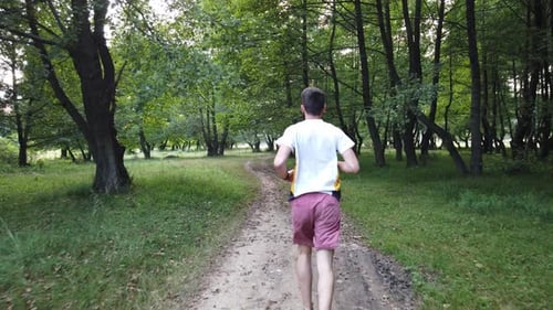 Young Caucasian male running in forest on a trail in summer. Man jogging cross country running on tr