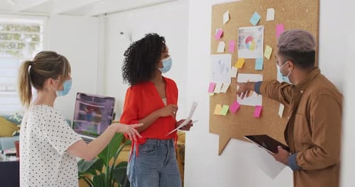 Office colleagues wearing face mask discussing over memo notes at office