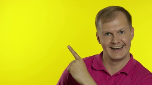 Portrait of Young Man Posing in Pink T-shirt. Happy Smiling Guy Pointing at Something with Hand