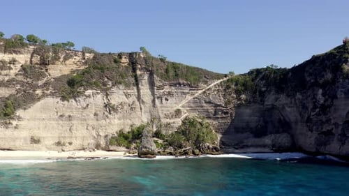 Sandy Diamond Beach in Nusa Penida island Indonesia with rock walls behind, Aerial dolly out reveal