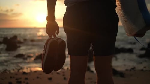 Silhouette Holding Surfboard and Shoes on Beach