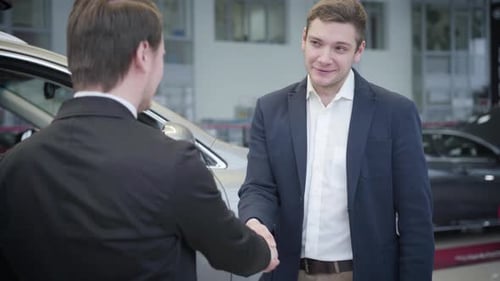 Portrait of Thankful Caucasian Man Shaking Dealer's Hand in Car Dealership