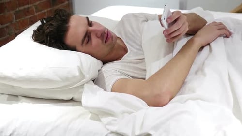 Mann im Bett surft nachts auf dem Smartphone