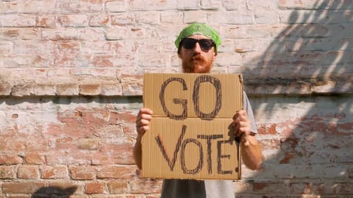 Adult Holds Go Vote Sign in Urban Setting