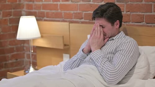 Hombre de mediana edad llorando sentado en la cama