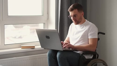 Man in Wheelchair Using Laptop by Window