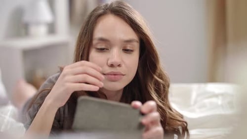 Young Woman Using Smartphone on Bed Indoors