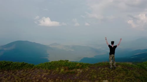 Aerial Drone View. Flying Around Young Man Standing on Top of the Mountain at Sunset