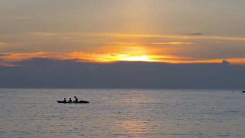 People Paddle Boat on Ocean During Sunset