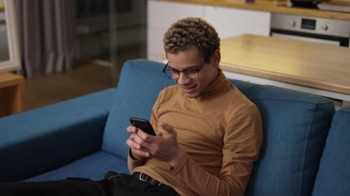 Man Uses Phone on Couch at Home