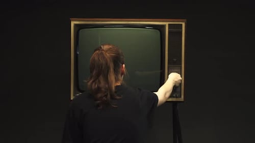 Young Woman Setting Up Channel on Old Retro Television on Black Background Searching for a Signal