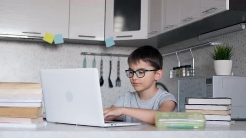 Junge mit Brille und Lehrbüchern macht Hausaufgaben in der Schule mit einem Laptop zu Hause. Online-Lernen