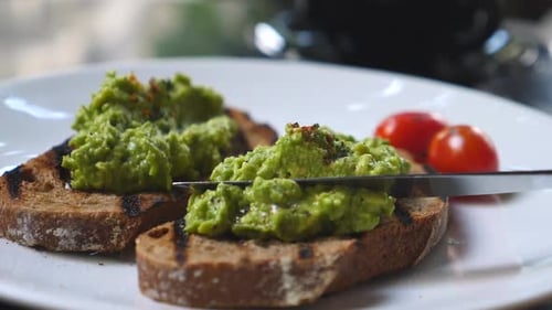 Knife Spreads Avocado on Toast with Tomatoes