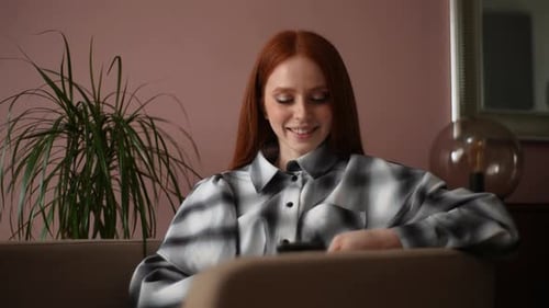Front View of Cheerful Attractive Young Woman Using Mobile Phone Looking on Screen of Phone Sitting