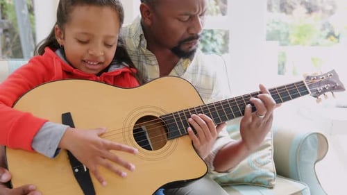 Child Learning Guitar from Father on Couch