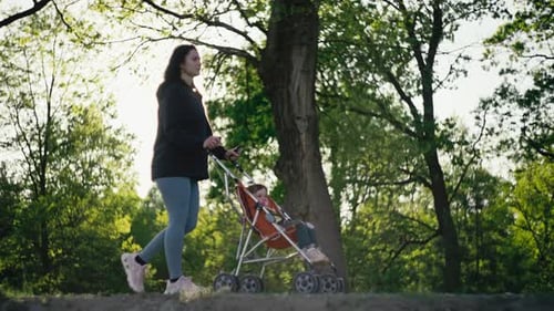 Mom Walks with a Stroller in the Park