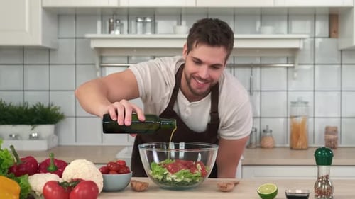 Chef masculino agrega aceite de oliva a la ensalada vegana mientras está de pie en la cocina en casa