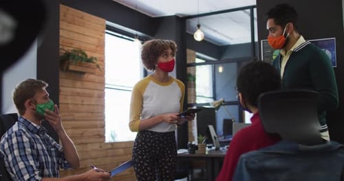Diverse colleagues wearing face masks discussing together at modern office