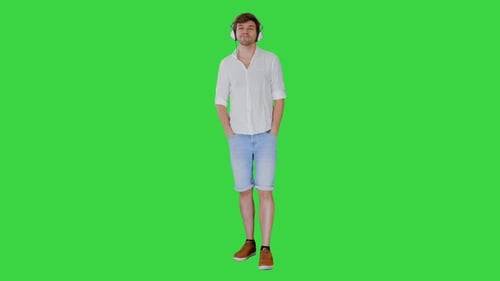 Casual Young Man in Headphones Listening To Music and Enjoying It Closing His Eyes on a Green Screen