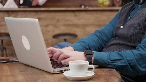 Man Typing on Laptop with Coffee in Cafe